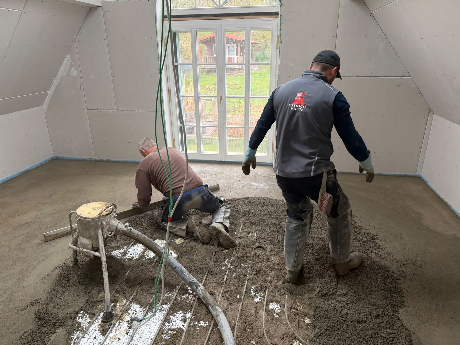 Zwei Estrichleger bringen im Dachgeschoss den Estrich ein und ziehen ihn ab