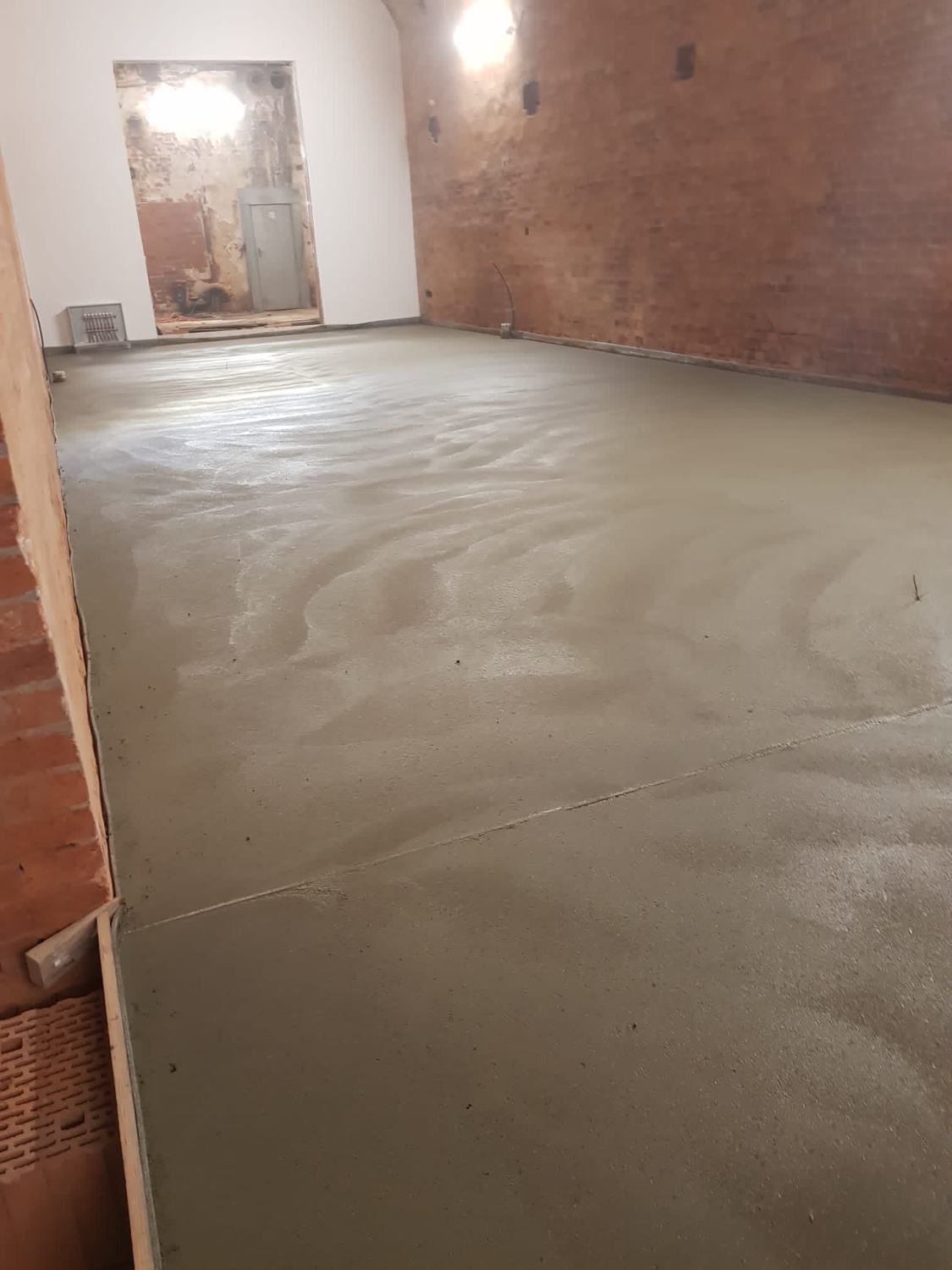 Frisch abgezogener Estrich in einer Halle mit Ziegelwand