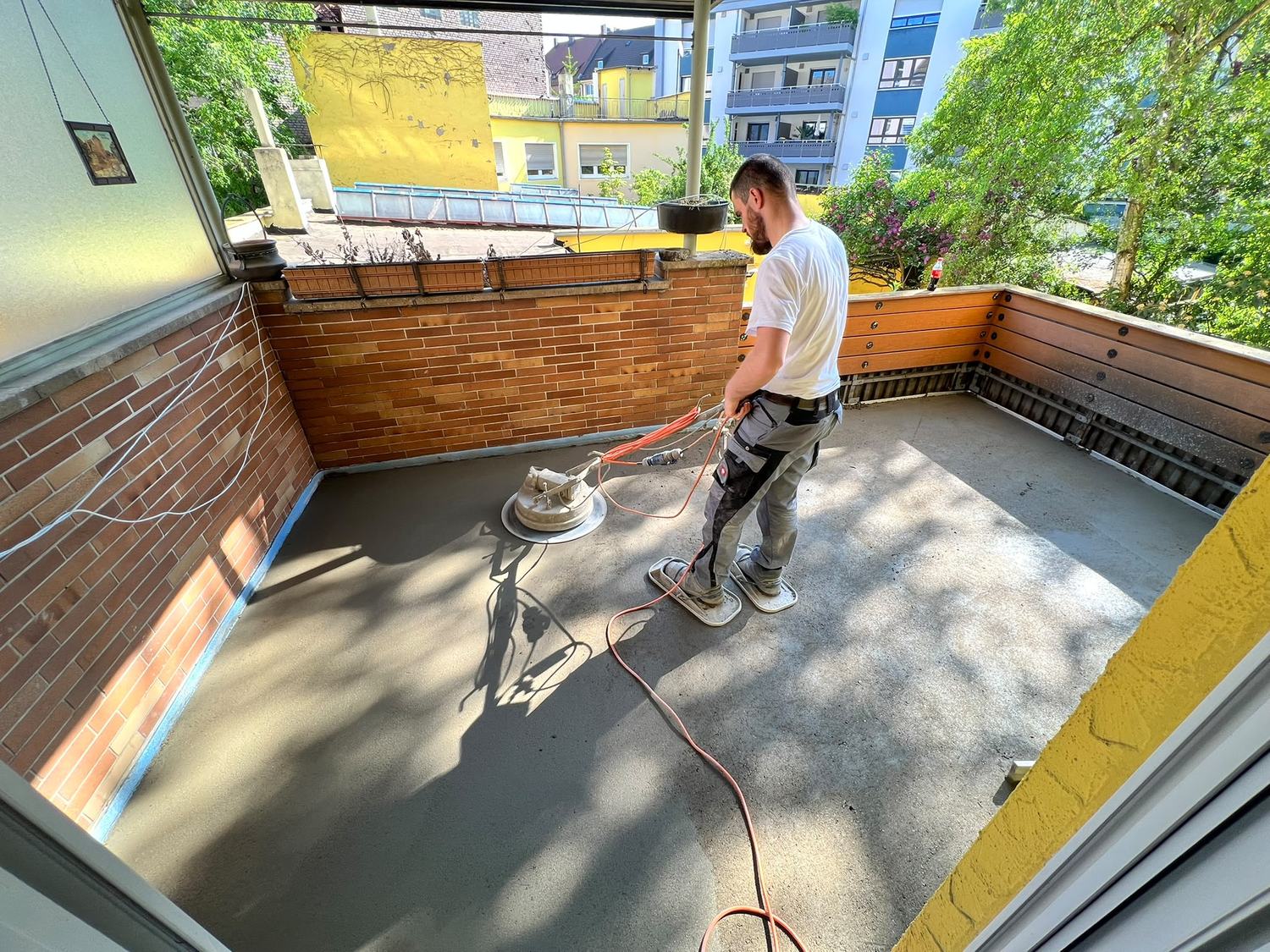 Estrichleger glättet mit der Maschine eine Fläche vor einer Ziegelwand